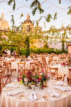 an outdoor event with tables and chairs covered in white tablecloths, lights strung from the ceiling