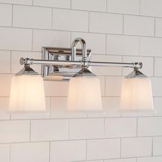 three light bathroom fixture in chrome finish with white glass shades on brick wall behind it