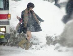 a woman walking in the snow next to a bus