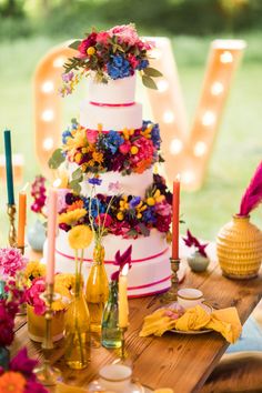 a multi - tiered wedding cake with colorful flowers and candles sits on a wooden table