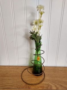 a green vase with white flowers in it on a wooden table next to a wall