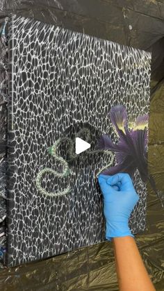 a person in blue gloves painting a wall with animal print on it and another hand holding up a purple flower