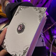 a person holding a white book with a pink jewel in the middle and purple lighting behind it