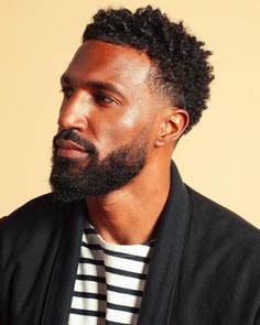 a close up of a person with a beard wearing a striped shirt and black blazer