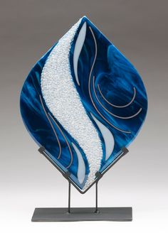 a blue and white glass sculpture sitting on top of a metal stand in front of a gray wall