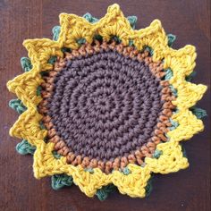 a crocheted sunflower is shown on a brown table top with green and yellow accents