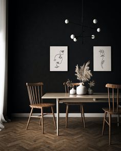 a dining room with black walls and wood flooring, two paintings on the wall