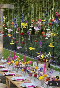 a long table with flowers hanging from it's ceiling and plates on the table