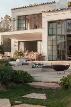 an outdoor patio with chairs and tables in front of a large white house that is surrounded by greenery