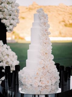 a wedding cake with white flowers on it and black candles in front of the cake