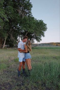 a man and woman standing in the middle of a field hugging each other with trees in the background