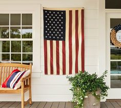 an american flag hanging on the side of a white house next to a potted plant