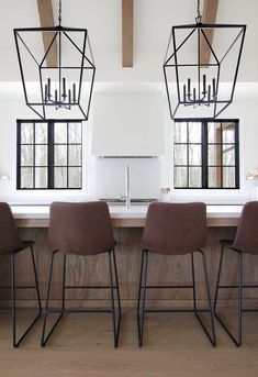 two brown chairs sitting in front of a kitchen island with lights hanging from the ceiling