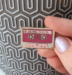 a hand holding a pink and white pin with an old school cassette design on it