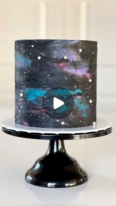 a black and blue cake with stars on it is sitting on a metal stand in front of a white wall