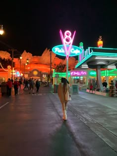 a woman walking down the street in front of a building with neon lights on it