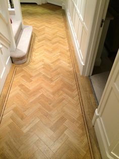 an empty hallway with wooden flooring and white trim on the walls, leading to another room