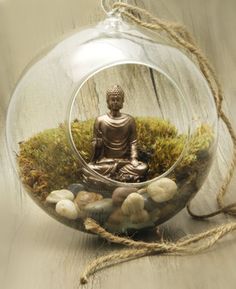 a glass ornament with a buddha statue in the center surrounded by rocks and grass