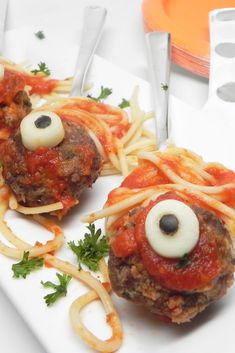 two spaghetti balls with googly eyes on them sitting on a white plate next to silverware