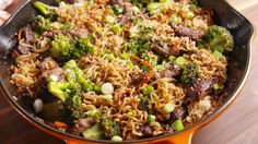 a skillet filled with noodles, meat and broccoli on top of a wooden table