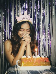 a woman sitting in front of a cake with lit candles on it and wearing a tiara