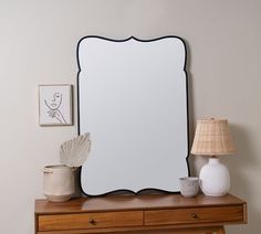 a mirror sitting on top of a wooden dresser next to a lamp and vases