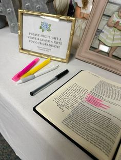 an open book sitting on top of a table next to some pens and pencils