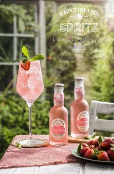 two bottles of pink lemonade sit on a table with strawberries