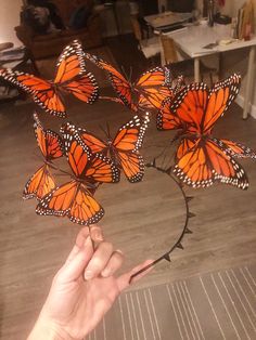 a hand is pointing at a bunch of orange butterflies on a wire sculpture in the shape of a circle