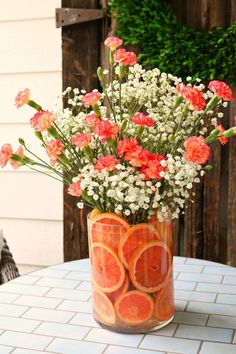 a vase filled with orange slices and flowers on top of a white tiled table next to a wooden fence