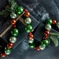 two presents wrapped in green and gold paper with christmas decorations around them on a black surface