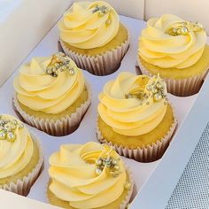 six cupcakes in a white box with yellow frosting and pearls on top