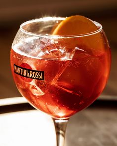 a close up of a drink in a wine glass with ice and an orange slice