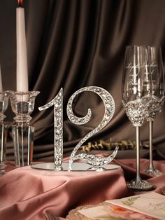 two wine glasses sitting on top of a table next to a silver number twenty candle holder