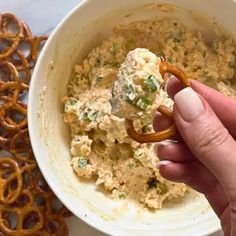 a hand holding a pretzel over a bowl of dip and pretzels