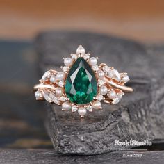 an emerald and white pearl ring on top of a piece of stone with pearls around it