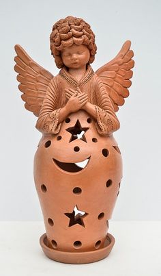 an angel figurine sitting on top of a ceramic jar with holes in it