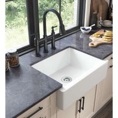 a white kitchen sink sitting under a window next to a counter top with black faucets