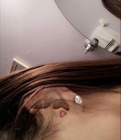 a woman with a red heart tattoo on her left ear and behind her ear is a mirror