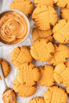 peanut butter cookies on parchment paper next to a bowl of peanut butter and a spoon