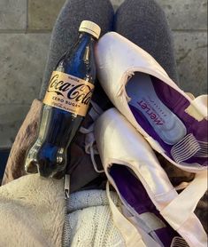 a bottle of coca cola sitting on top of someone's feet with their shoes