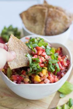 a person dipping a tortilla into a white bowl filled with fruit and veggies