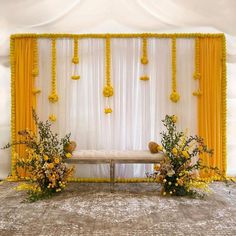 a decorated stage with yellow drapes and flowers on the side, along with two benches