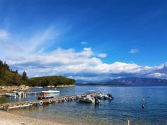 several boats are docked on the shore of a lake with mountains in the background and blue sky