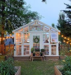 a small white greenhouse with lights on the roof and plants in pots around it's perimeter