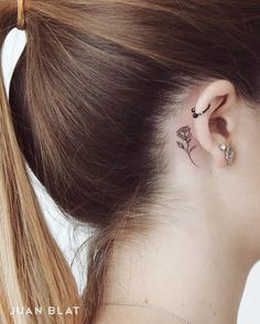 a woman's left ear has a small rose tattoo on the back of her right ear