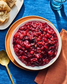 a bowl of cranberry sauce on a blue table cloth with bread in the background