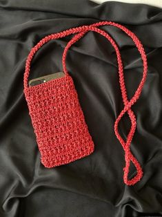 a crocheted red cell phone case sitting on top of a black cloth covered bed