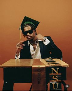 a man sitting at a desk with a graduation cap on and holding a pencil in his hand