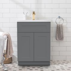 a bathroom with white tile and gray cabinet next to the bathtub, towel rack and sink